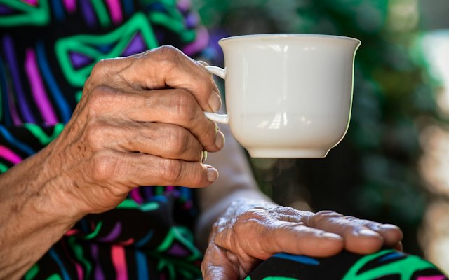 白いカップを持つ年配の人の手もと